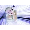 Pretty, young woman tanning her skin in a modern solarium (shallow DOF; color toned image)