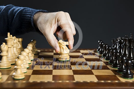 Hand moving a knight chess piece on wooden chessboard Hand moving a knight chess piece on wooden chessboard