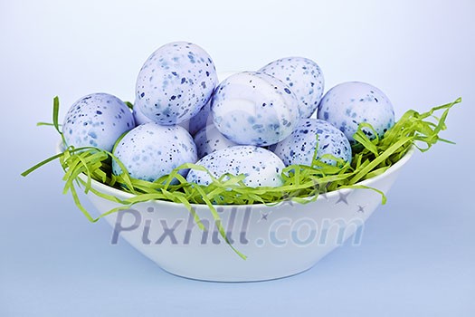 Many blue speckled easter eggs in bowl on green paper grass Many blue speckled easter eggs in bowl on green paper grass