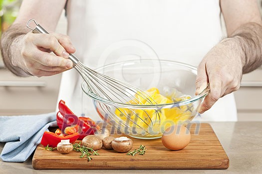 Closeup on man's hands whisking eggs in bowl for cooking omelet with vegetables Closeup on man's hands whisking eggs in bowl for cooking omelet with vegetables