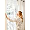 Happy woman looking out big bright window with curtains and blinds