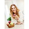 Portrait of smiling woman holding red apple leaning on countertop in kitchen at home