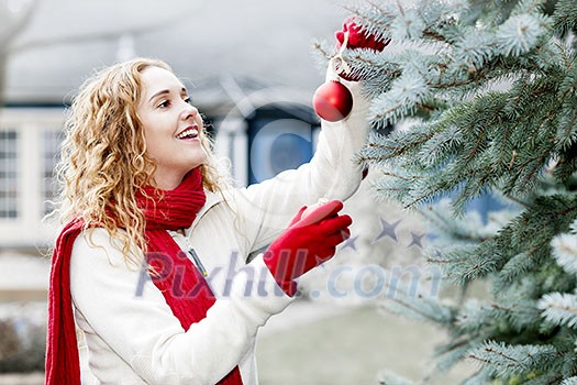 Portrait of smiling woman hanging Christmas ornaments on spruce tree outdoors in yard near home Portrait of smiling woman hanging Christmas ornaments on spruce tree outdoors in yard near home