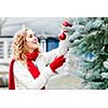 Portrait of smiling woman hanging Christmas ornaments on spruce tree outdoors in yard near home