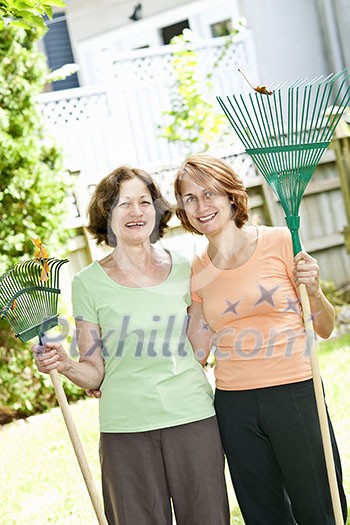 Mother and daughter holding rakes gardening outside Mother and daughter holding rakes gardening outside