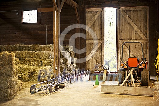 Interior of wooden barn with hay bales stacks and farm equipment Interior of wooden barn with hay bales stacks and farm equipment