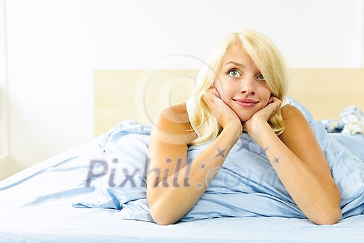 Happy blonde young woman laying in bed dreaming and smiling
