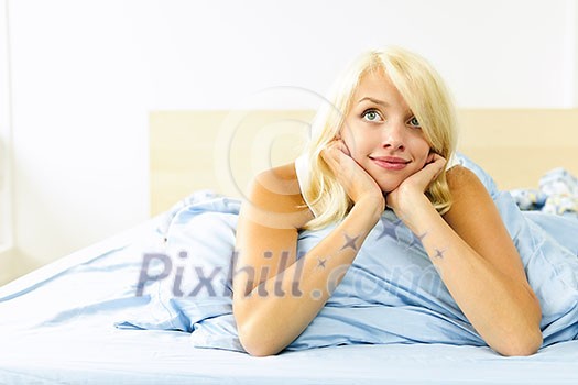Happy blonde young woman laying in bed dreaming and smiling