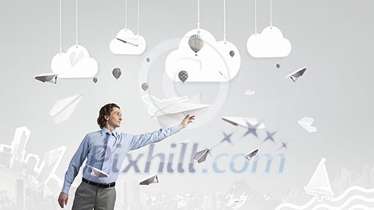 Young businessman in pile of books with paper plane in hand Young businessman in pile of books with paper plane in hand