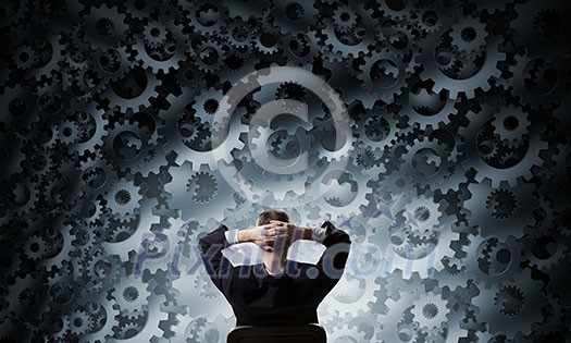 Young relaxed businessman sitting in chair and looking at gears mechanism Young relaxed businessman sitting in chair and looking at gears mechanism