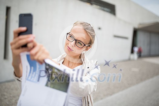 Pretty, female tourist taking a selfie picture while visiting a foreign city and its highlights landmarks, looking happy and relaxed. loving the travel (shallow DOF; color toned image)