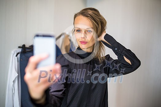 Young woman shopping in a fashion store, trying on some clothes she likes - taking a selfie picture with her smartphone in the cabin (color toned image; shallow DOF) Young woman shopping in a fashion store, trying on some clothes she likes - taking a selfie picture with her smartphone in the cabin (color toned image; shallow DOF)