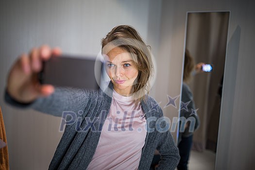Young woman shopping in a fashion store, trying on some clothes she likes - taking a selfie picture with her smartphone in the cabin (color toned image; shallow DOF) Young woman shopping in a fashion store, trying on some clothes she likes - taking a selfie picture with her smartphone in the cabin (color toned image; shallow DOF)