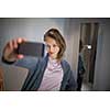 Young woman shopping in a fashion store, trying on some clothes she likes  - taking a selfie picture with her smartphone in the cabin (color toned image; shallow DOF)