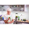 Senior woman cooking in the kitchen - eating and cooking healthy for her family; putting some potates in the oven, enjoying active retirement (shallow DOF; color toned image)