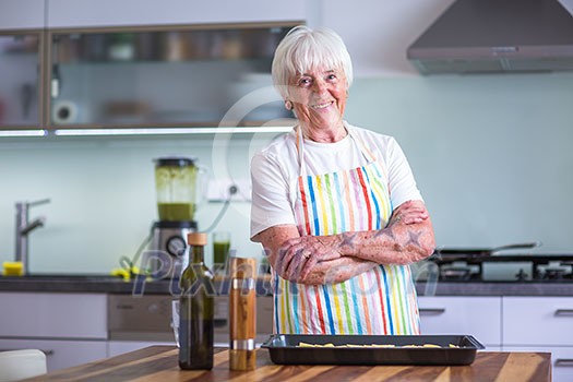 Senior woman cooking in the kitchen - eating and cooking healthy for her family; putting some potates in the oven, enjoying active retirement (shallow DOF; color toned image) Senior woman cooking in the kitchen - eating and cooking healthy for her family; putting some potates in the oven, enjoying active retirement (shallow DOF; color toned image)