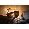 Young woman using her tablet computer in her bed late at night (color toned image; shallow DOF)