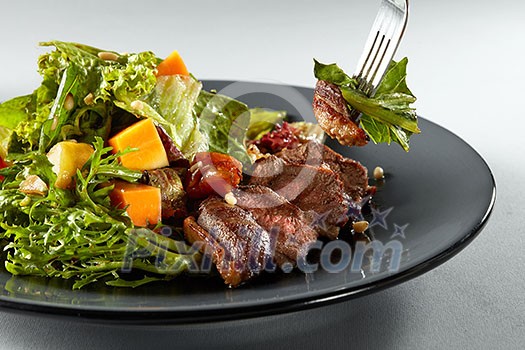 salad with pumpkin, grilled meat duck and fresh green salad on a plate and fork with salad salad with pumpkin, grilled meat duck and fresh green salad on a plate and fork with salad