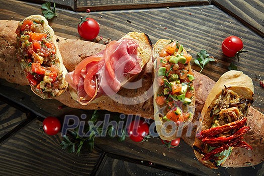 Italian crostini with various toppings serving on baguette on wooden black background, top view Italian crostini with various toppings serving on baguette on wooden black background, top view