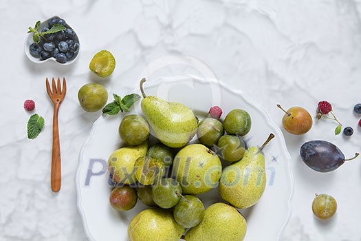 fresh plums and pears on a white plate on white background