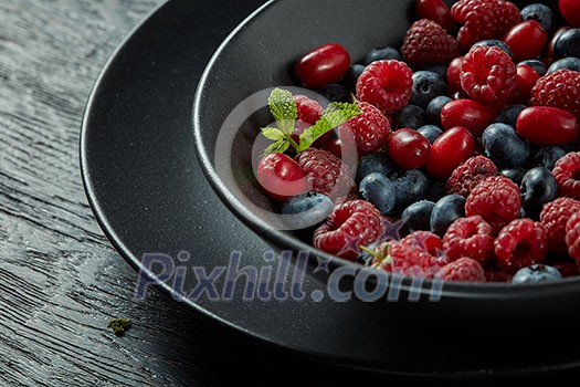 black plate with fresh healthy berries and mint on a dark background black plate with fresh healthy berries and mint on a dark background