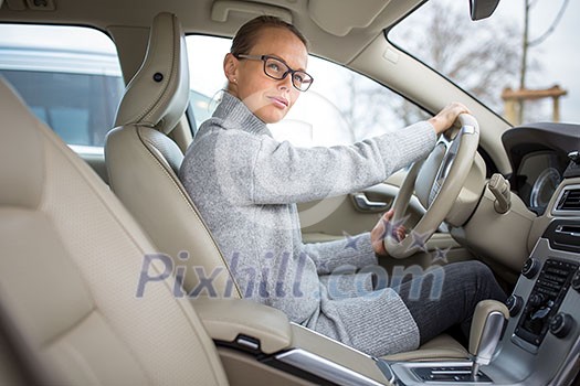 Woman driving a car - female driver at a wheel of a modern car, looking happy, smiling with a relaxed smile (shallow DOF; color toned image) Woman driving a car - female driver at a wheel of a modern car, looking happy, smiling with a relaxed smile (shallow DOF; color toned image)