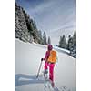 Pretty, young woman snowshoeing in high mountains, enjoying splendid winter weather with abundance of snow