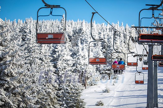 Ski lift with skiers being carried up the hill on a lovely, sunny winter day