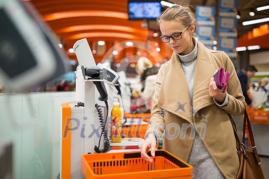 Pretty, young woman shopping for some fruit and smoothie in a grocery store; paying for the goods at the self-service register (color toned image) Pretty, young woman shopping for some fruit and smoothie in a grocery store; paying for the goods at the self-service register (color toned image)