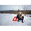 Young woman setting up a warning triangle and calling for assistance after her car broke down in the middle of nowhere on a freezing winter day