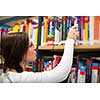 College/university campus - Pretty young female student in library looking for a book (color toned image; shallow DOF)