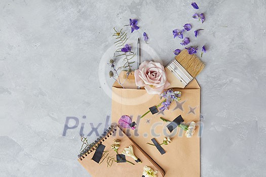 Composition of envelope over grey background with many ingredients in it. Notebook decorated with flowers. Copy space for your ideas and emotions. Composition of envelope over grey background with many ingredients in it. Notebook decorated with flowers. Copy space for your ideas and emotions.