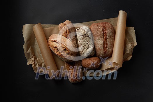 Mix fresh bread on parchment on black background in still life. Mix fresh bread on parchment on black background in still life.