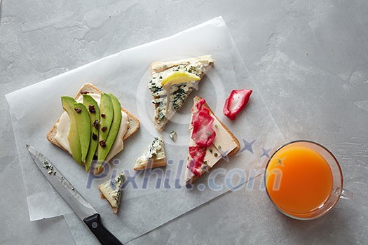 Top view of delicious sandwiches with cheese, avocado, etc. Different kinds of sandwiches for tasting or having break isolated on table. Glass of orange juice not far from it. Top view of delicious sandwiches with cheese, avocado, etc. Different kinds of sandwiches for tasting or having break isolated on table. Glass of orange juice not far from it.