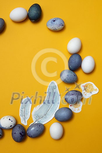 eggs and painted feathers on a yellow background, flat lay eggs and painted feathers on a yellow background, flat lay