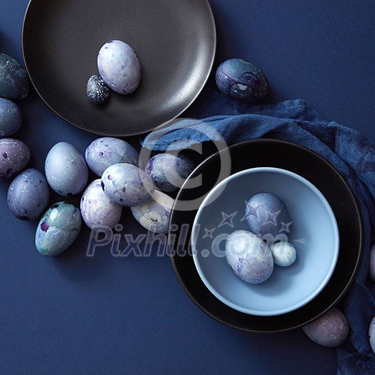 Easter eggs on dark plate, blue napkin on a dark blue background, flat lay