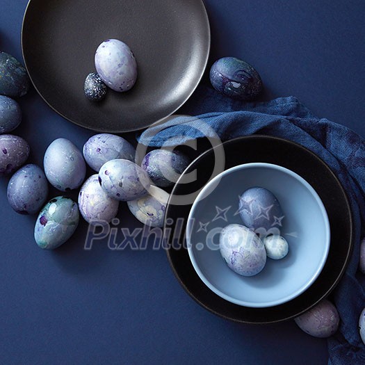 Easter eggs on dark plate, blue napkin on a dark blue background, flat lay Easter eggs on dark plate, blue napkin on a dark blue background, flat lay