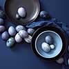 Easter eggs on dark plate, blue napkin on a dark blue background, flat lay