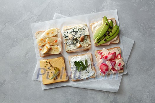 Different types of toast with cheese, vegetables on parchment on a concrete gray background Different types of toast with cheese, vegetables on parchment on a concrete gray background