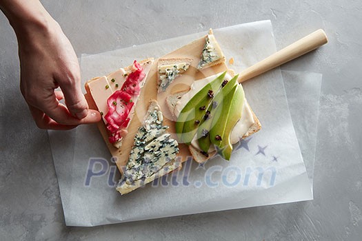 Human hand takes a sandwich with cheese and vegetables from a wooden board on a concrete background Human hand takes a sandwich with cheese and vegetables from a wooden board on a concrete background
