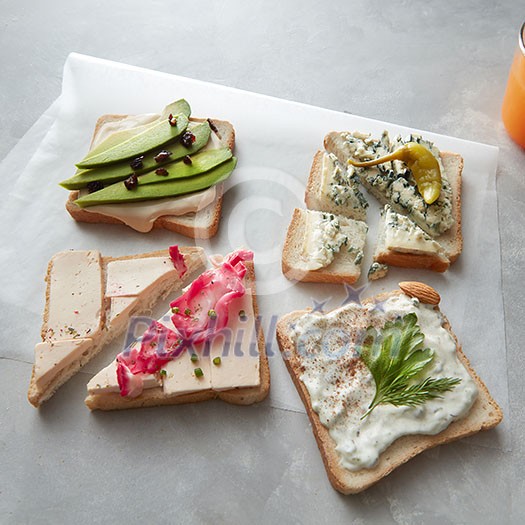 Slices of sandwiches with cheese and vegetables on parchment on a concrete background Slices of sandwiches with cheese and vegetables on parchment on a concrete background