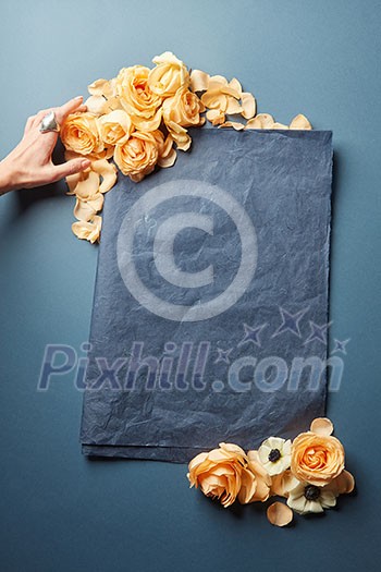 Female hand decorating blank sheet of paper with flowers. Empty frame for text Female hand decorating blank sheet of paper with flowers. Empty frame for text