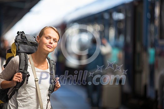 Pretty young woman boarding a train/having arrived to her destination, waiting for her friends to pick her up (color toned image)