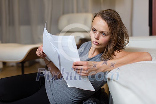 Pretty, young woman studying for an exam/ going through some paperwork in her lovely living room at night, looking rather tired Pretty, young woman studying for an exam/ going through some paperwork in her lovely living room at night, looking rather tired