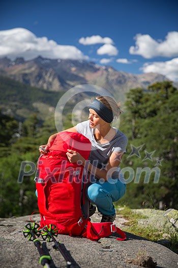 Pretty, female hiker in high mountains packing her backpack Pretty, female hiker in high mountains packing her backpack