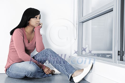 Depressed black woman sitting against wall on floor looking out window Depressed black woman sitting against wall on floor looking out window