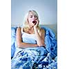 Sleepy blonde woman yawning sitting up in bed