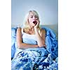 Sleepy blonde woman yawning sitting up in bed