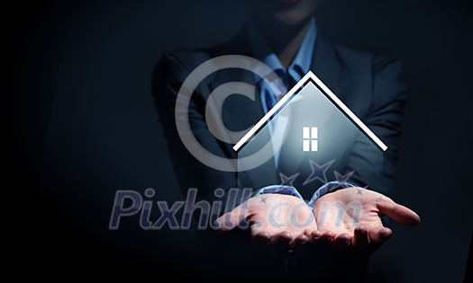 Close up of businesswoman holding real estate icon in palm on dark background Close up of businesswoman holding real estate icon in palm on dark background