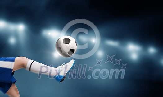 Leg of kid boy in blue uniform on soccer stadium kicking ball Leg of kid boy in blue uniform on soccer stadium kicking ball